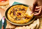 A bowl of sweet potato pepita dip with a person dipping a piece of flatbread