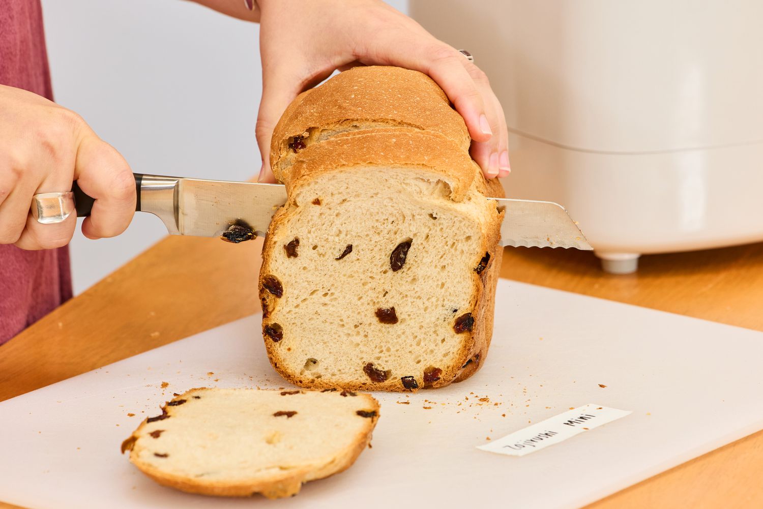 A person cutting a loaf of bread made in the Zojirushi Home Bakery Mini Breadmaker on a cutting board