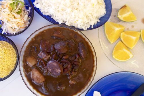 Overhead view of feijoada with all the accompaniments: farofa, rice, orange wedges, and a cabbage slaw.