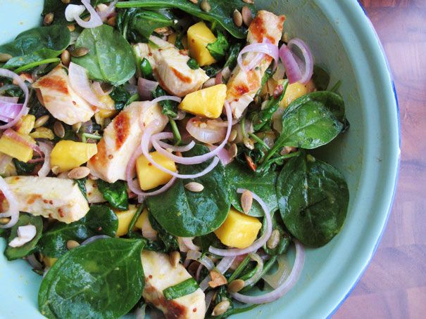 Overhead closeup of grilled chicken and spinach salad with honey mustard, served in a blue bowl.