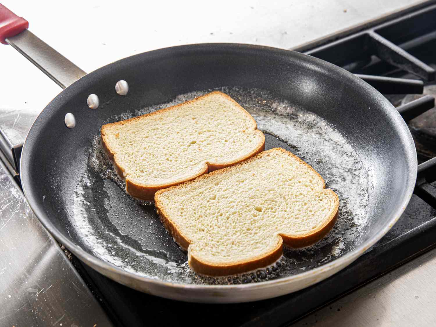 Two pieces of bread being toasted in butter in a pan