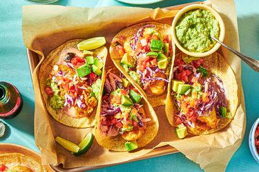 Overhead view of four Baja fish tacos on a parchment-lined tray with guacamole and lime