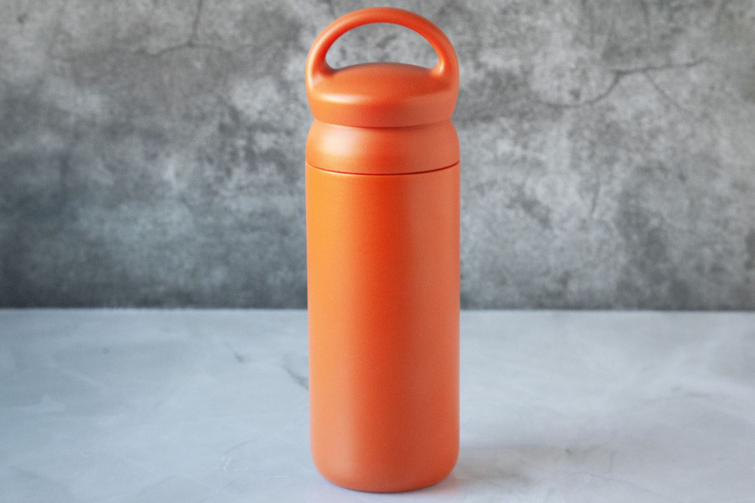 An orange travel mug on a marble kitchen countertop.