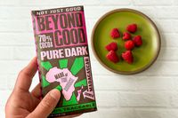 A person holding the Beyond Good Pure Dark 70% Bar next to a plate of raspberries