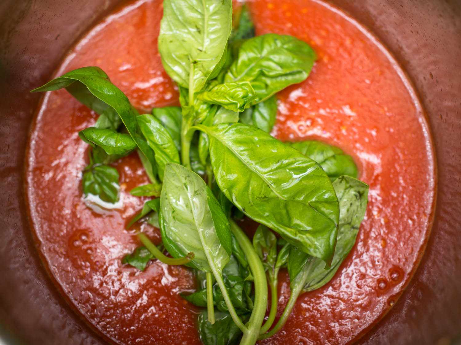 Basil stems added to the top of a pot of tomato sauce.