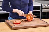 A person slices a tomato using the Mercer Culinary 8-Inch Genesis Chef's Knife