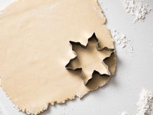 A starshaped cookie cutter on rolled dough sprinkled with flour on a surface