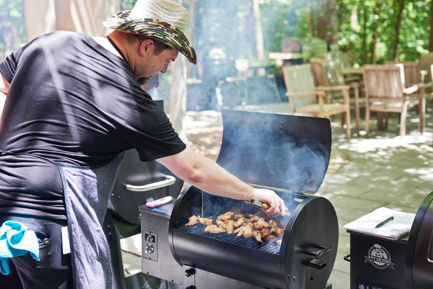 a person using tongs to retrieve chicken wings cooking on a small Traeger grill