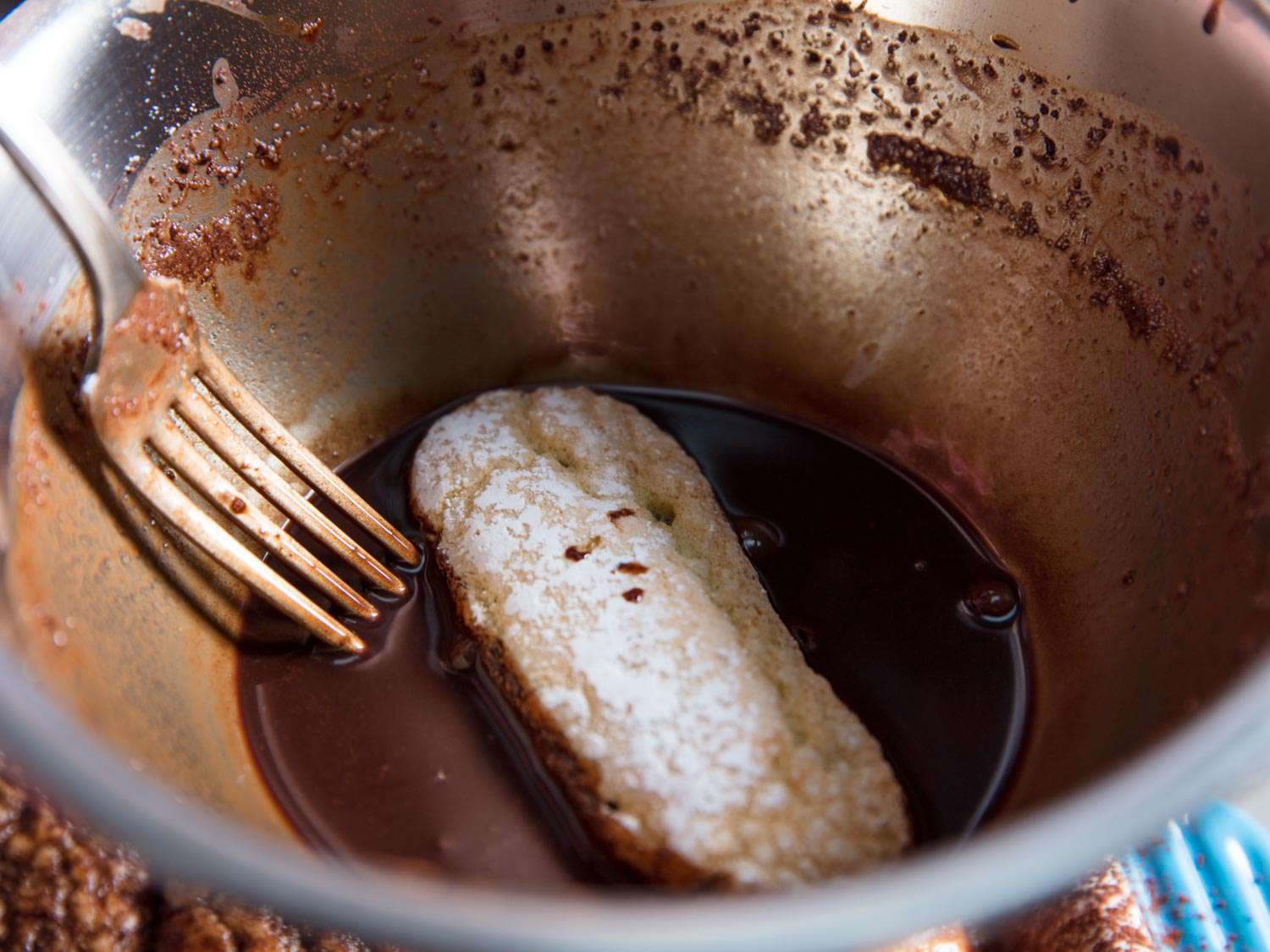 A close-up of dipping a ladyfinger into the last bit of coffee chocolate syrup.