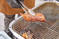 Tongs lifting cooked chicken off of PK Grills Original PK300 Grill & Smoker 