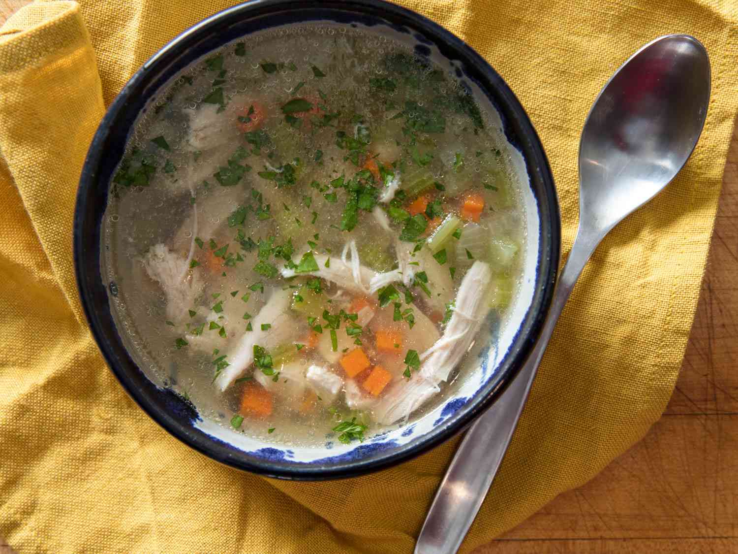 A bowl of chicken soup with a spoon beside it.