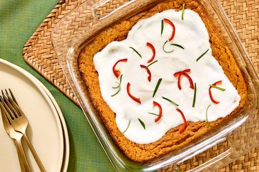 Overhead angle of whole squash souffle in glass baking dish, on a green fabric and woven placemat. Plate and forks on the side 