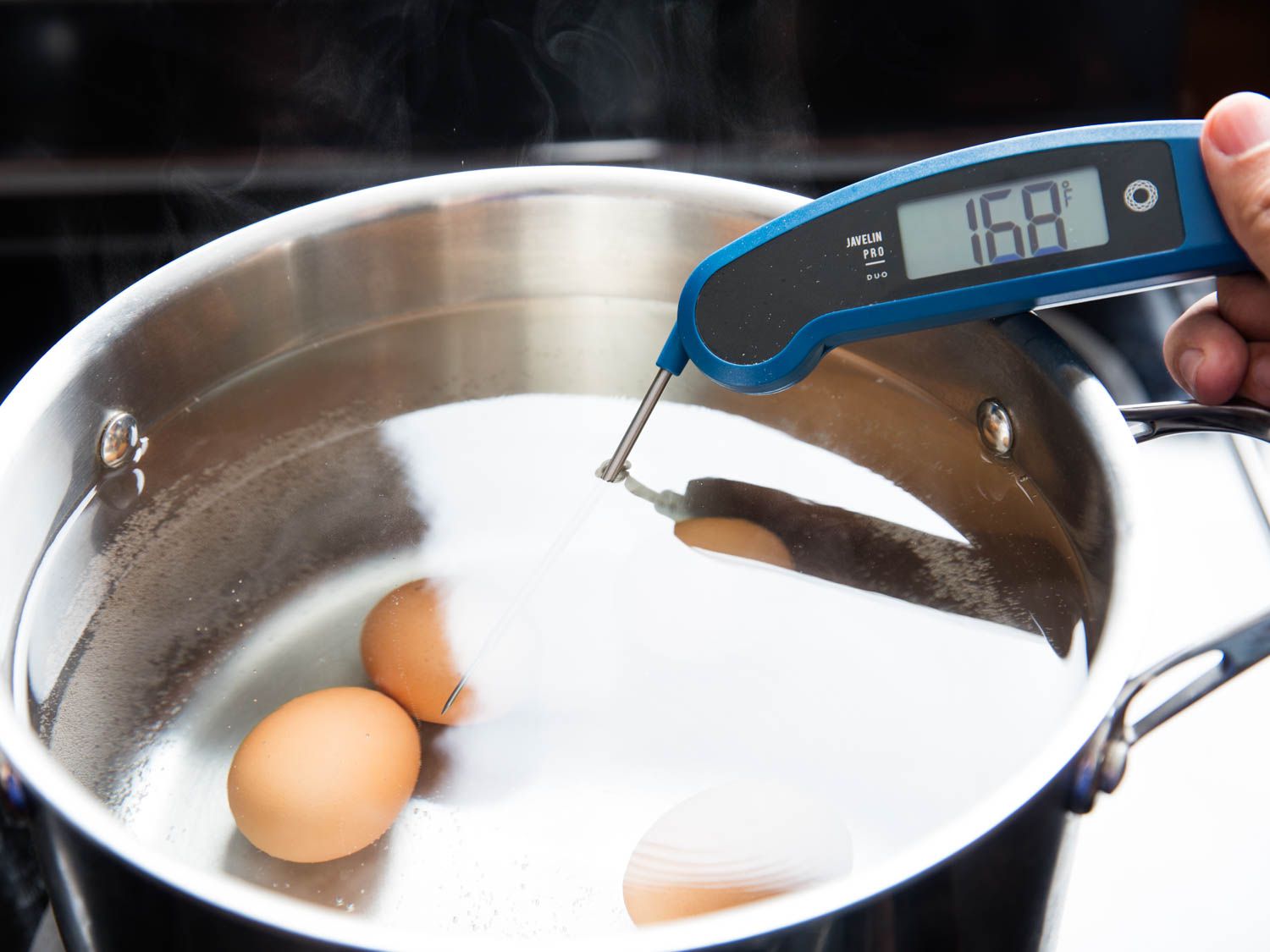 Eggs have been lowered into a large pot full of water. An instant read thermometer registers that the water is 168 degrees Fahrenheit.