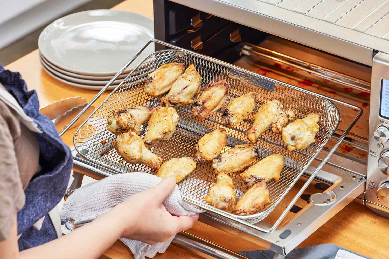 A hand removing cooked chicken wings from the Breville the Smart Oven Air Fryer