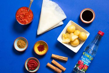 A collection of ingredients used in Moroccan cooking, including preserved lemon, rose water, cinnamon, saffron, Ras el Hanout, harissa, and a sheet of warqa pastry 