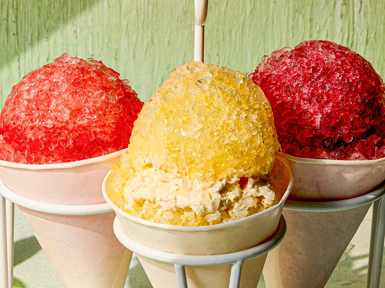 Three snow cones in paper cups one yellow in the center and red ones on the sides