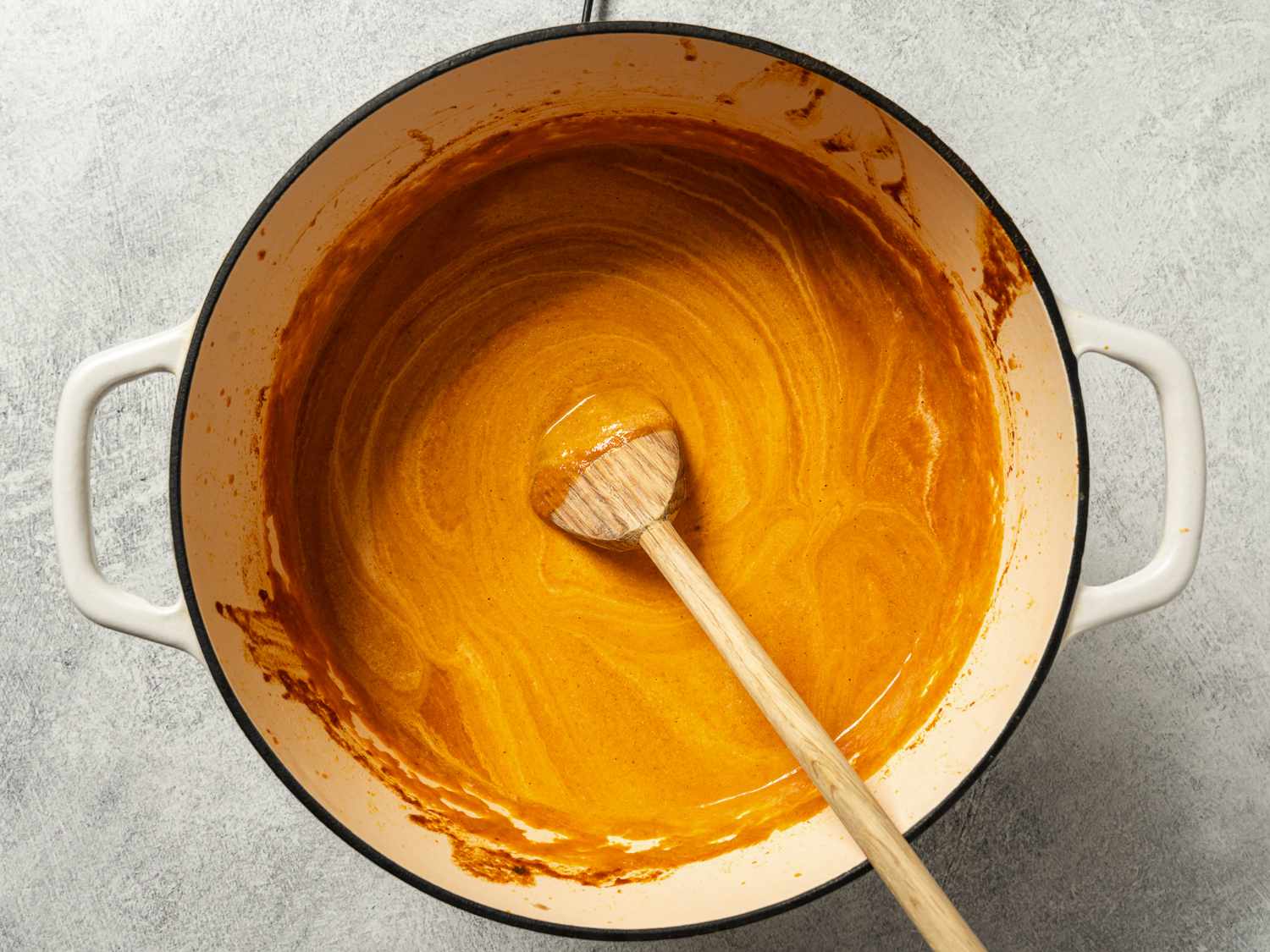 A Dutch oven holding the pureed sauce, which has now had cream and lemon juice stirred on. There is a large wooden spoon resting in the center of the pot.