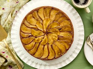 Upsidedown pear cake arranged on a white plate accompanied by tableware and a cup of coffee