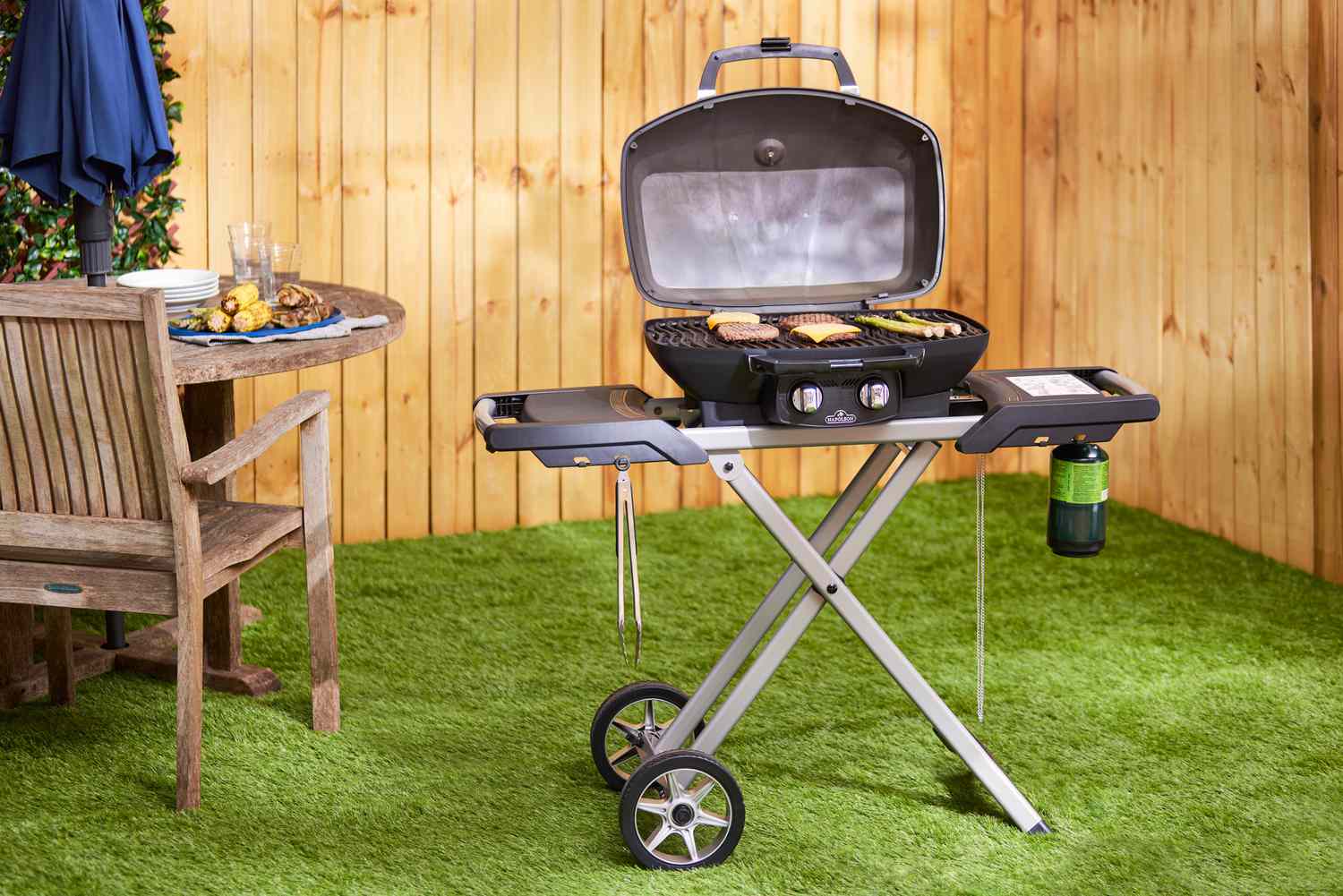The Napoleon Travel gas grill on a grass surface next to a picnic table.