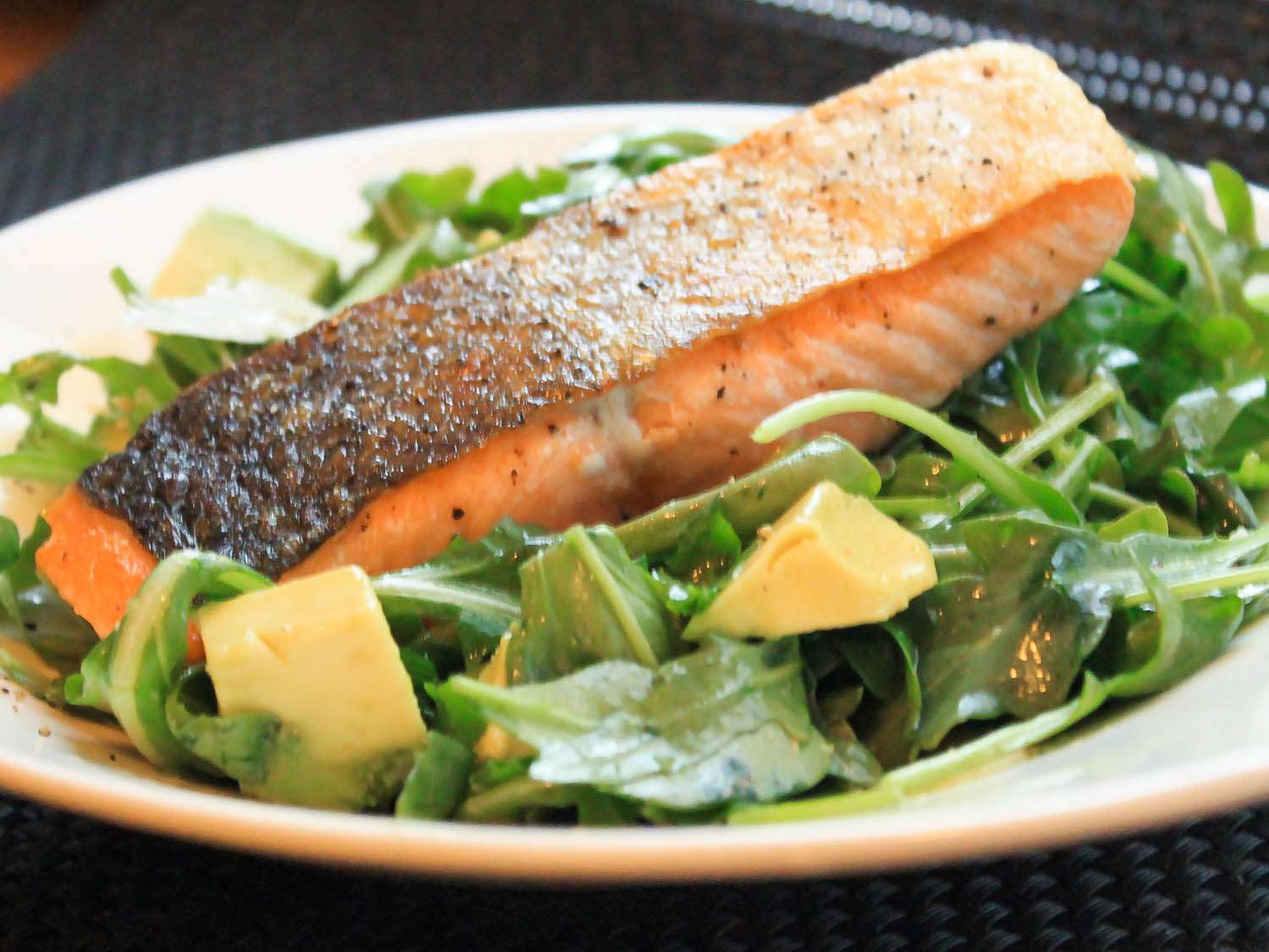 A piece of pan-roasted salmon plated on bed of arugula salad with avocado chunks.