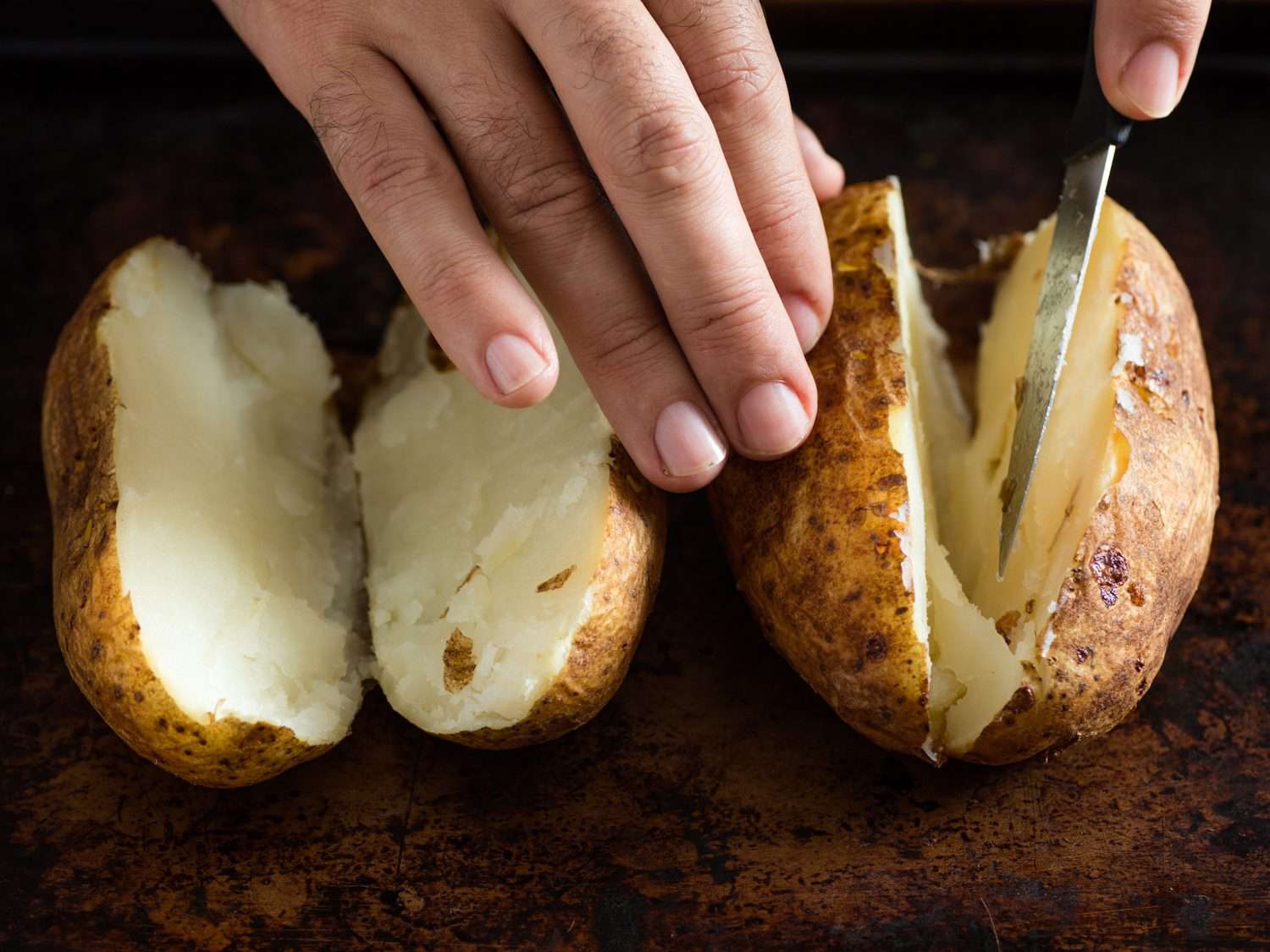 Using a paring knife to cut two potatoes in half.