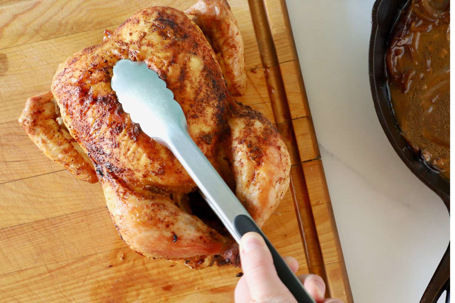 Hand picking up a whole chicken using the OXO Good Grips 12-Inch Tongs
