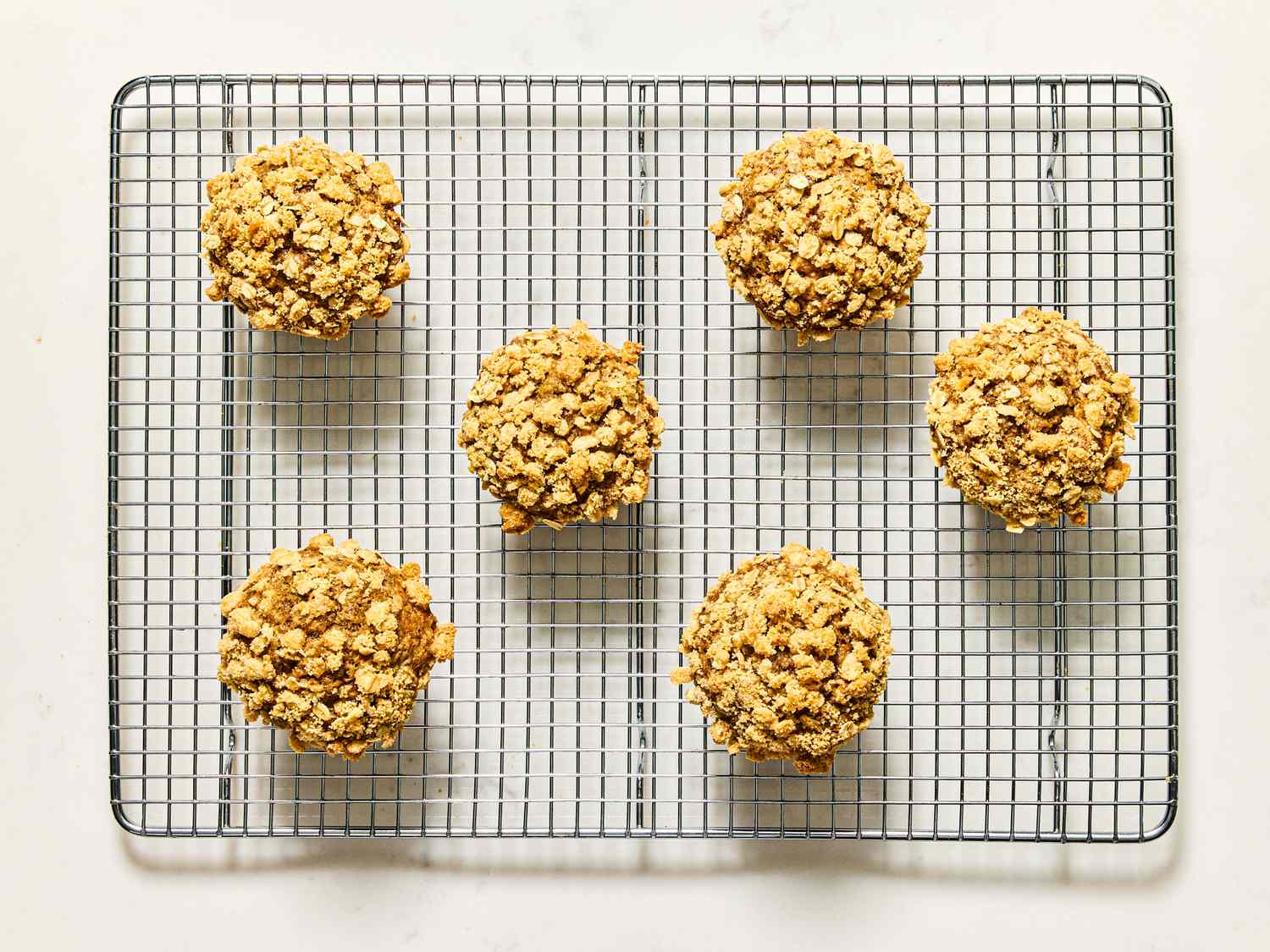 Six banana oatmeal muffins topped with crumble sitting on a cooling rack
