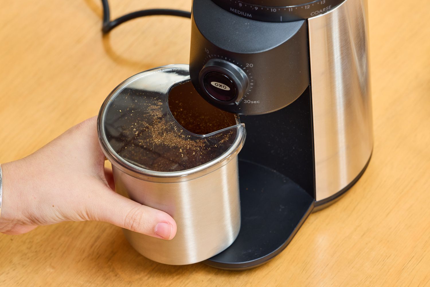 A person removes a cup of coffee grinds from the OXO Brew Conical Burr Coffee Grinder