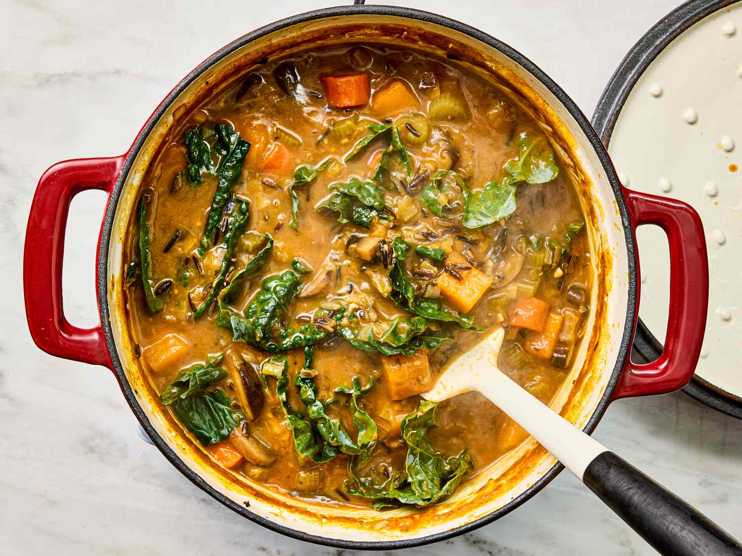A pot of soup with vegetables and leafy greens a ladle rests inside