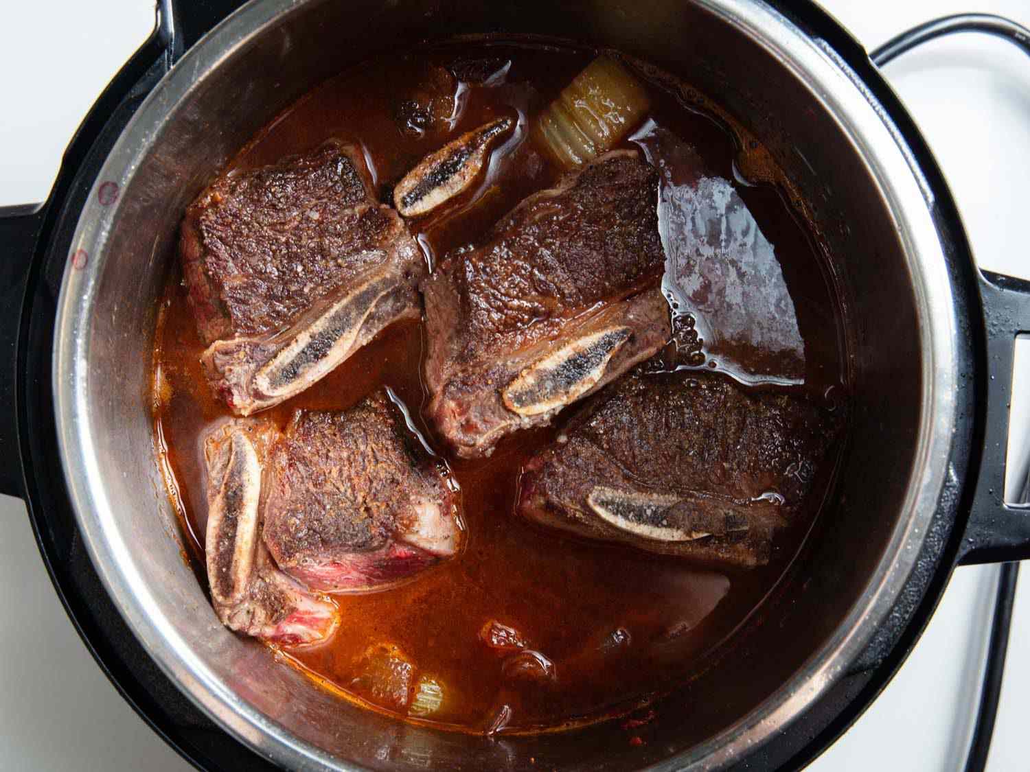 Browned beef short ribs in a pressure cooker with red wine and aromatics before braising