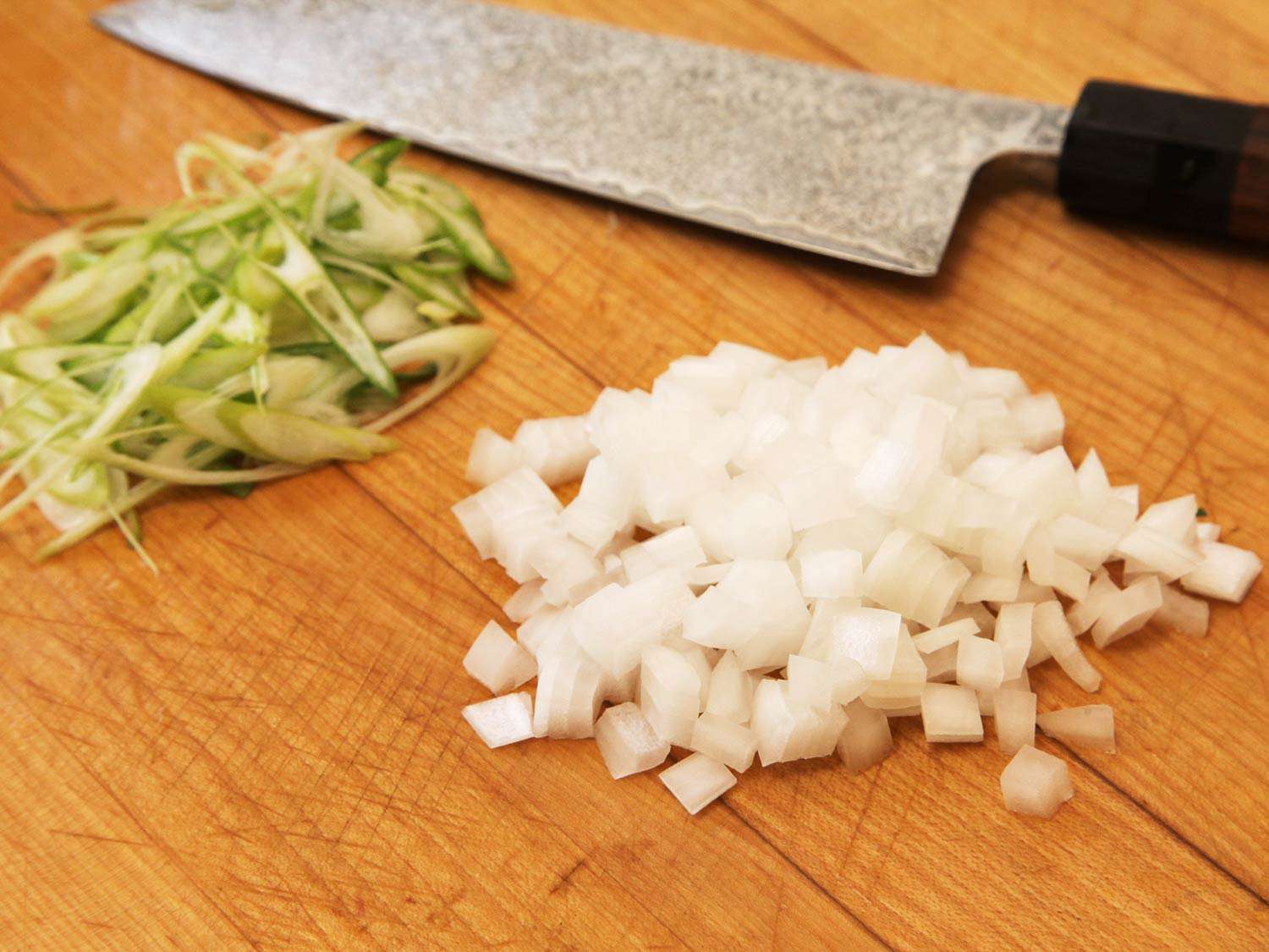 A cutting board containing finely chopped white and green onions with a knife off to the side.