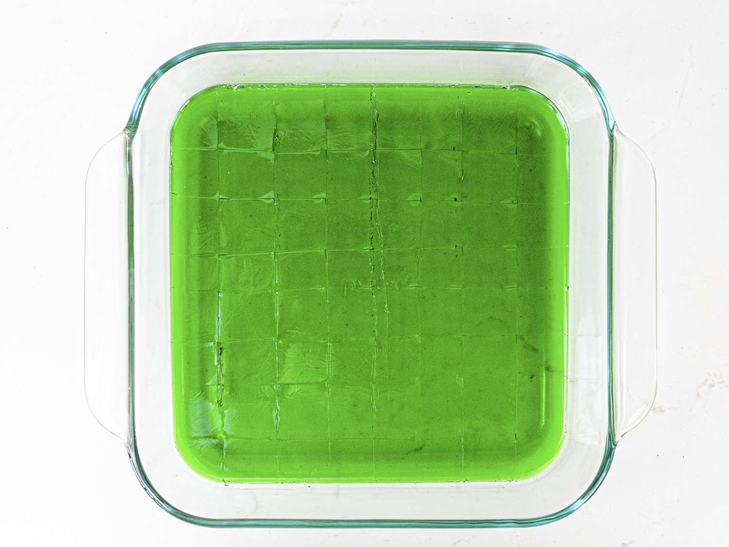 Green gelatin mixture cut into squares in a clear pan