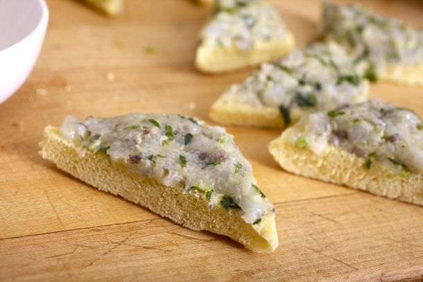 The shrimp mixture spread on pieces of potato bread, which are sitting on a wood cutting board.