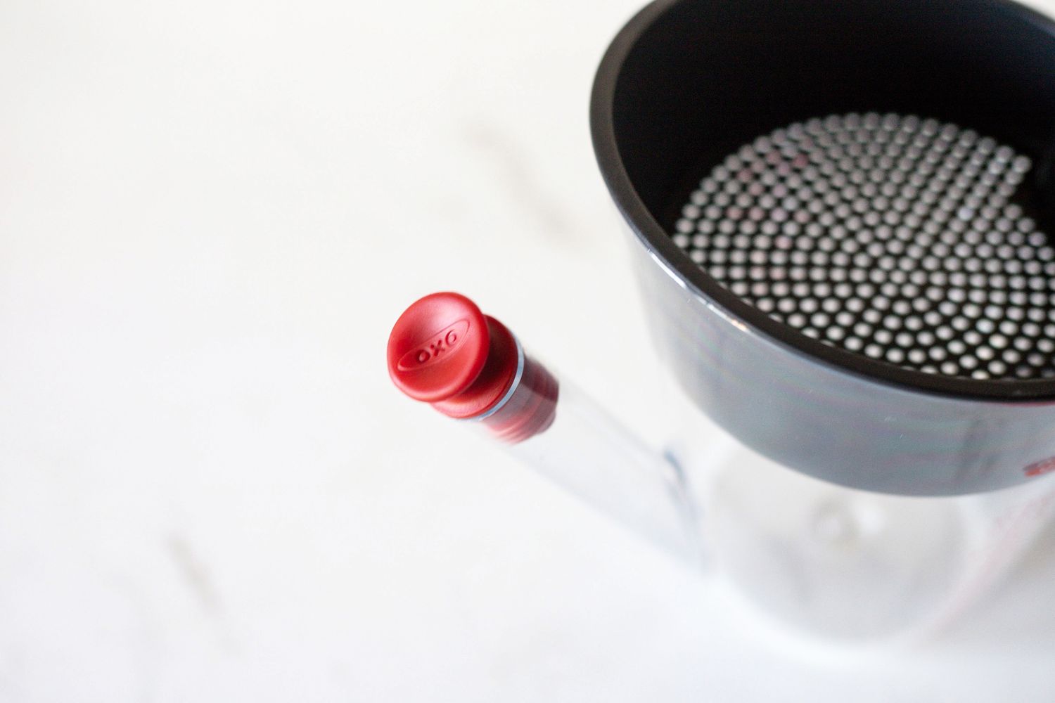 A closeup of a kitchen tool with a red OXObranded handle and a perforated black top