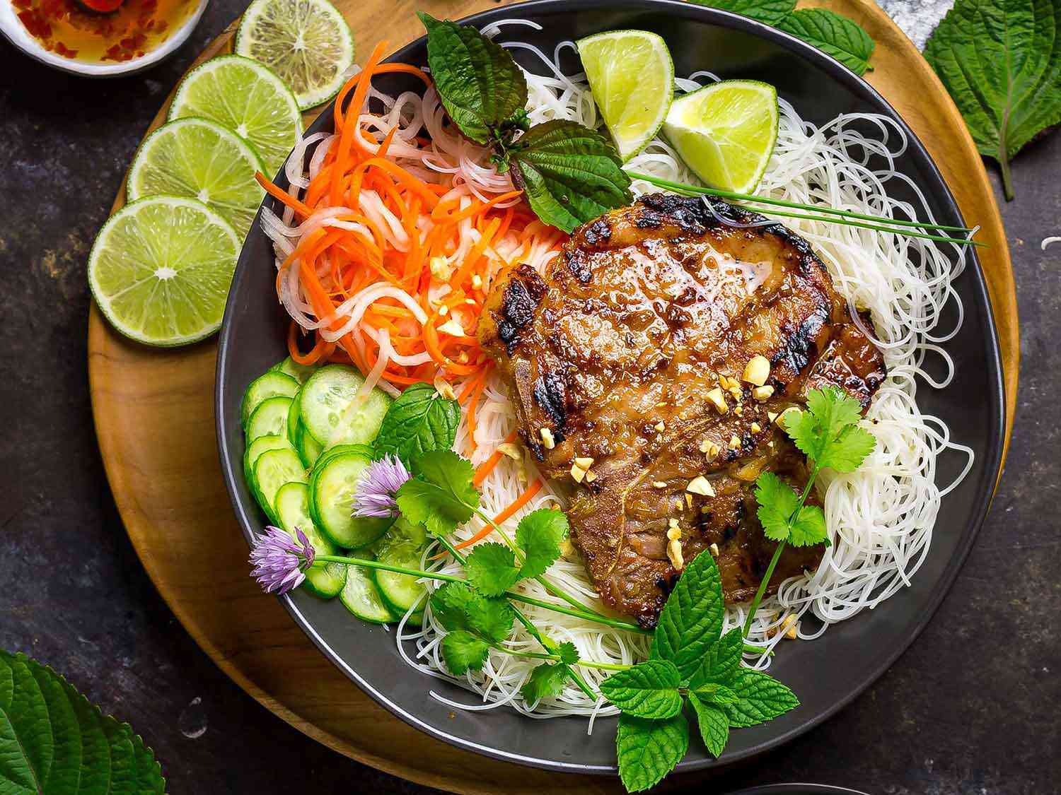 A finished bowl of the noodles, pork chops, and vegetables, garnished with herbs and crushed peanuts.
