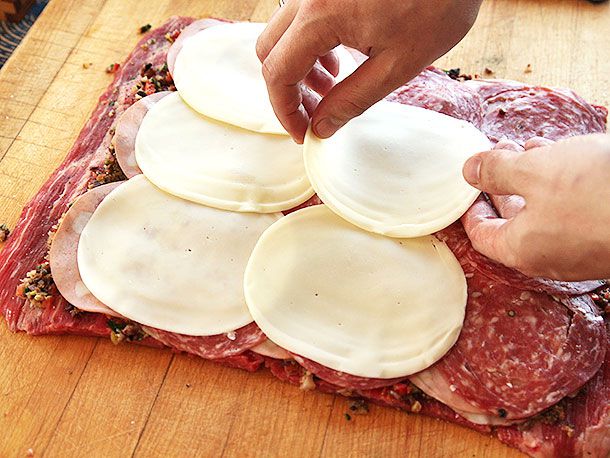 Layering slices of round white cheese onto a large piece of flattened flank steak