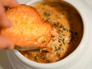 Closeup of a toasted slice of baguette being dipped in French onion soup cheese dip.