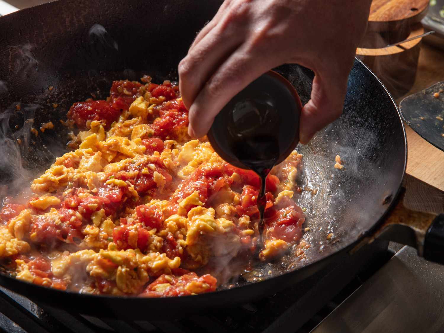 Black vinegar being added to tomato and egg mixture in wok.