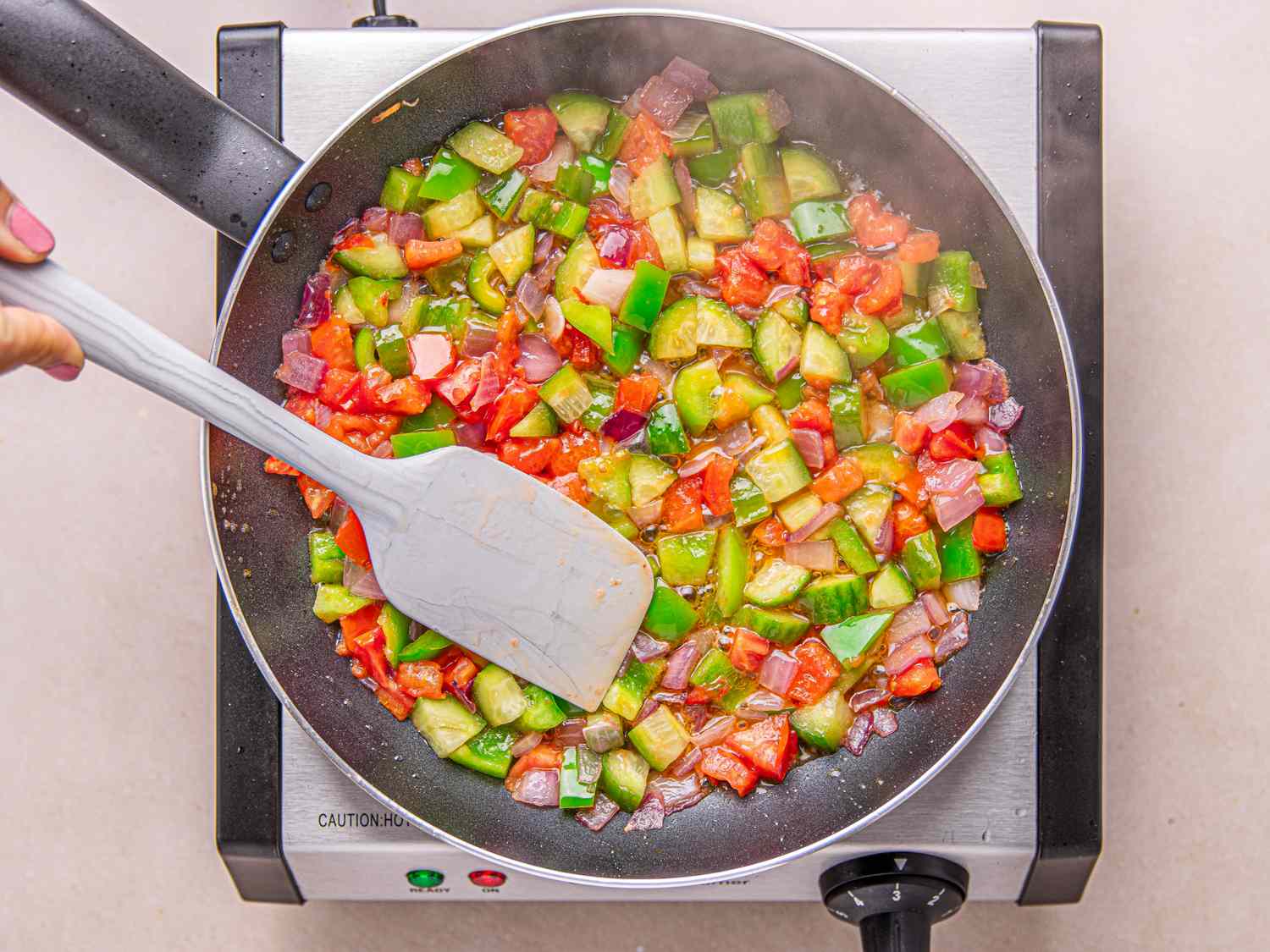 Vegetables being cooked in a frying pan including tomatoes peppers and onions