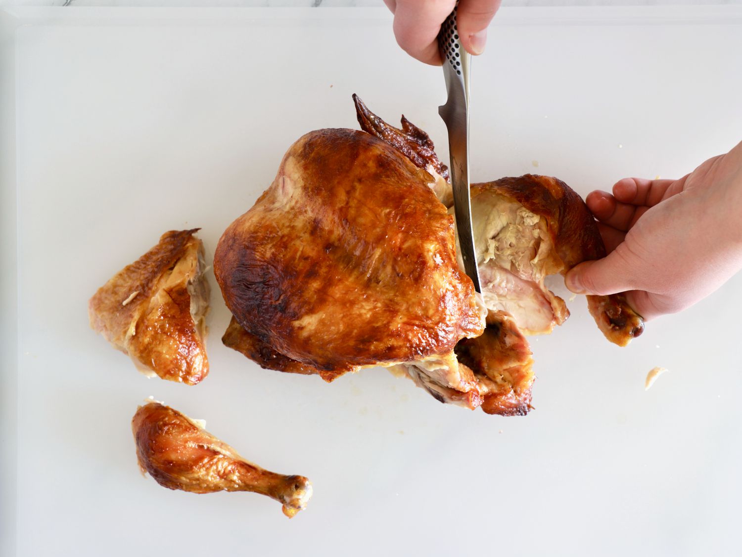 A person using the Global boning knife to carve a roasted chicken.