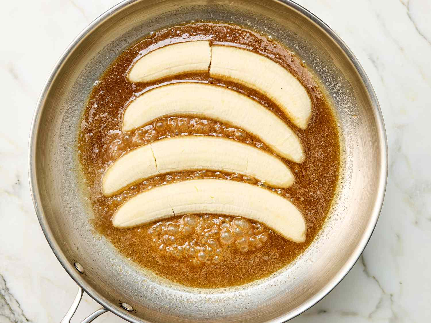Banana slices cooking in a caramel sauce in a metal pan
