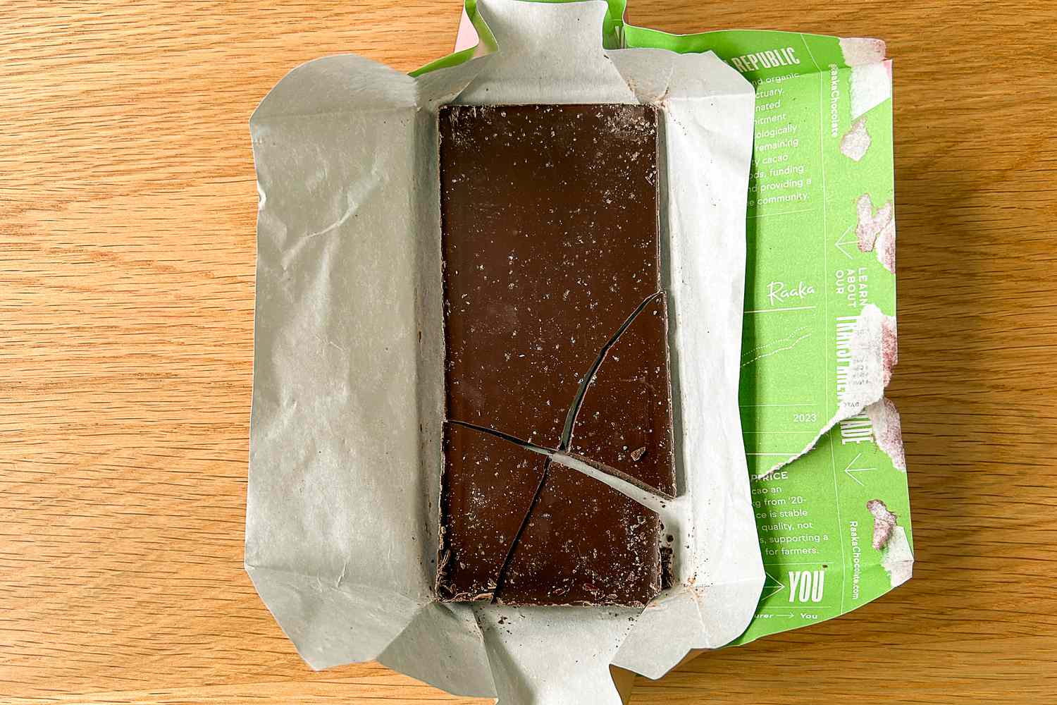 The Raaka Pink Sea Salt Dark Chocolate Bar unwrapped on a wood surface