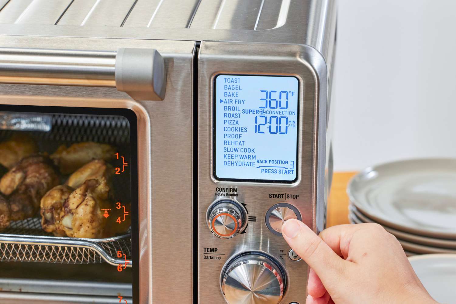A thumb pressing a button on the Breville the Joule Oven Air Fryer Pro
