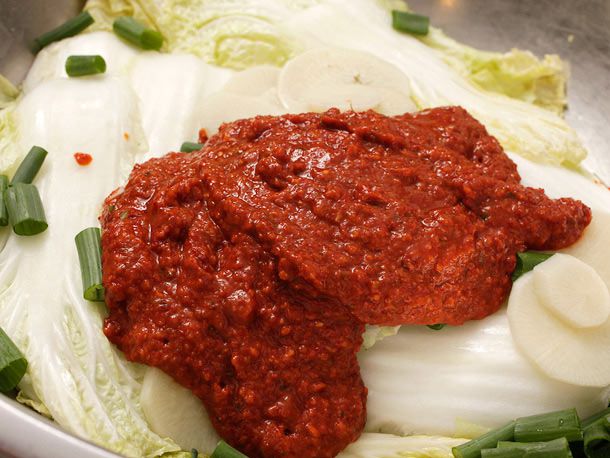 The chile paste is added to the wilted cabbage, daikon, and scallion greens.