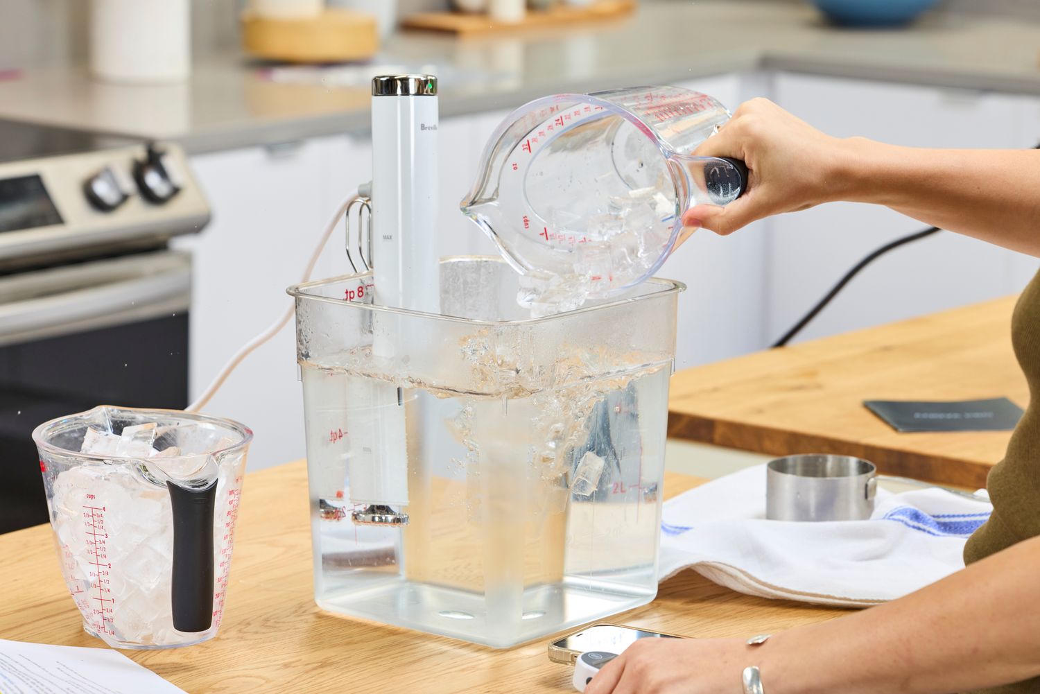 Pouring a liquid containing ice into a clear water container to cook using the Breville Joule Turbo Sous Vide Machine