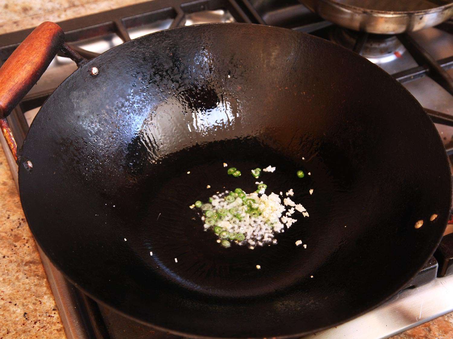 Minced garlic and sliced chile are cooked in a wok.