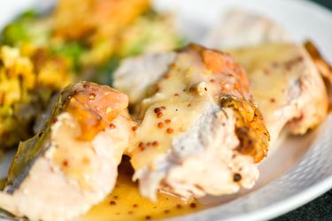 A plate of smoked turkey breast slices with white wine and mustard gravy, all on a white plate with cornbread dressing in the background.. 