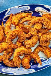 Southern Fried Shrimp on a blue printed plate, with dip, and sparkling water, and a blue textile. 