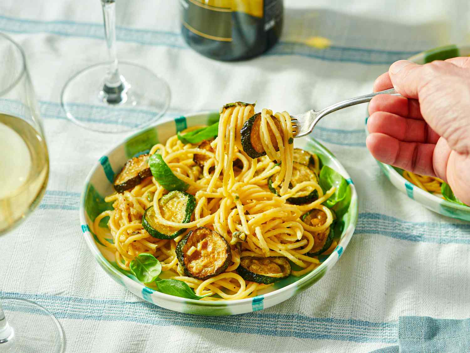 A dish of spaghetti with vegetables being twirled on a fork