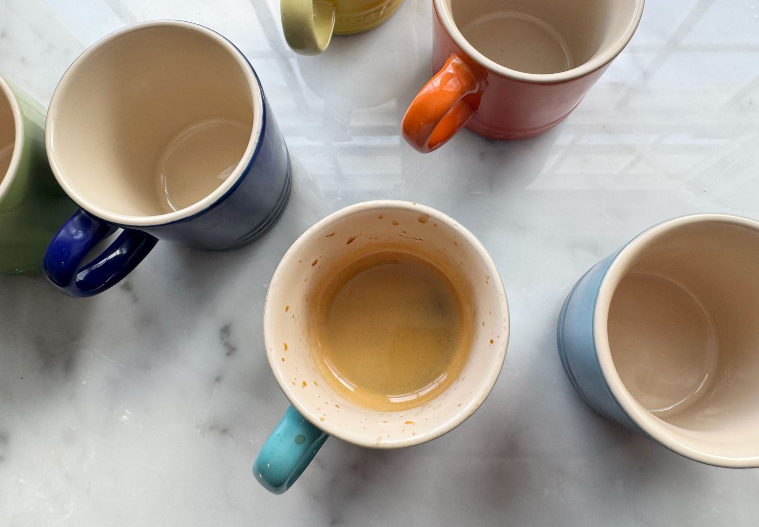 A Le Creuset espresso cup with espresso in it beside others that are empty.